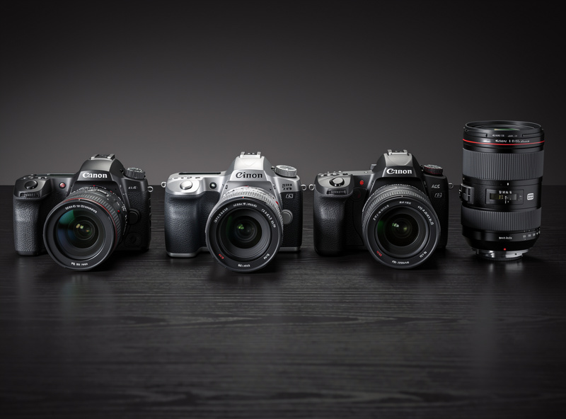 Four camera bodies from different manufacturers arranged on a wooden table with lenses beside them