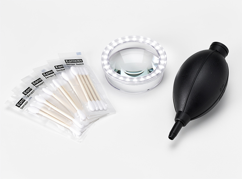 Camera sensor cleaning kit with swabs, loupe, and rocket blower on white surface