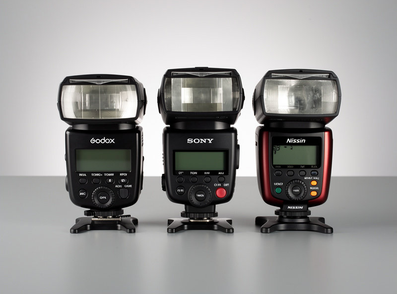 Multiple speedlight flash units — Godox, Sony, Nissin — side by side comparison