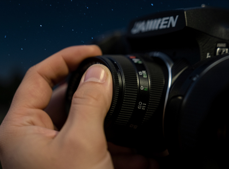 Close-up of a hand adjusting the manual focus ring on a camera lens at night