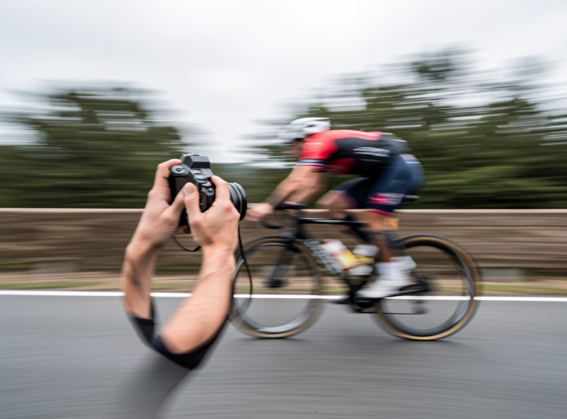 A photographer panning a mirrorless camera to track a fast-moving cyclist with motion blur