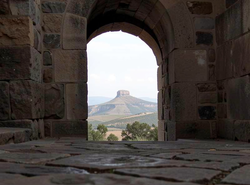 A scenic view photographed through a stone archway that frames the distant landmark, with textured foreground stones adding depth, demonstrating frame-within-a-frame composition