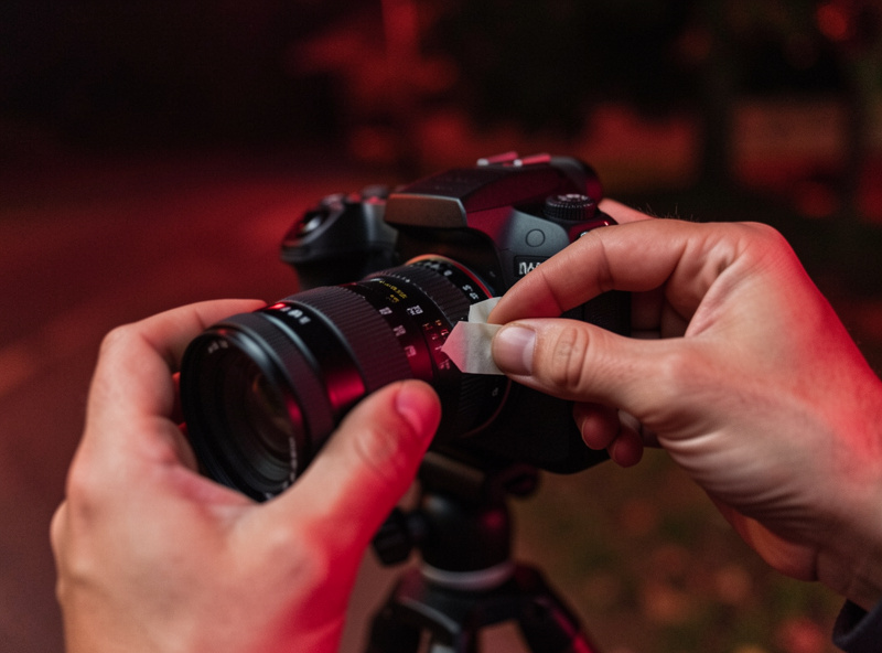 A photographer taping a lens focus ring in place after setting infinity focus at night