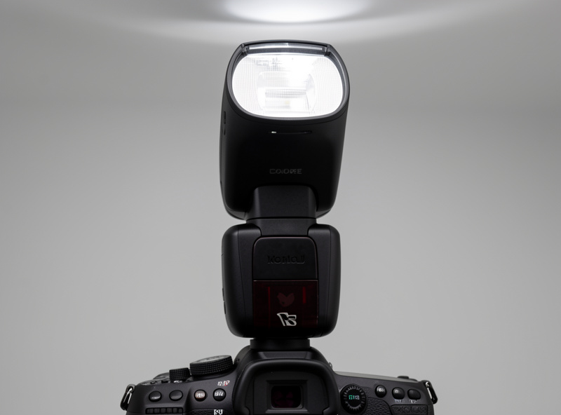 A speedlight mounted on a camera hot shoe with the head tilted upward to bounce light off the ceiling