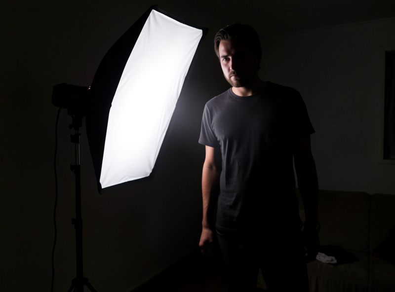 A single off-camera speedlight on a light stand firing through a softbox toward a portrait subject