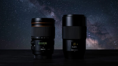 A fast wide prime lens beside a wide-angle zoom lens for astrophotography on a dark surface