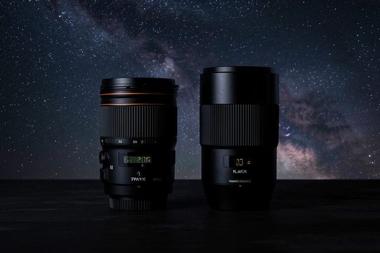A fast wide prime lens beside a wide-angle zoom lens for astrophotography on a dark surface