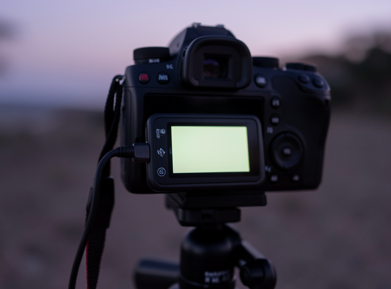 Close-up of a programmable intervalometer with an LCD screen plugged into a mirrorless camera on a tripod