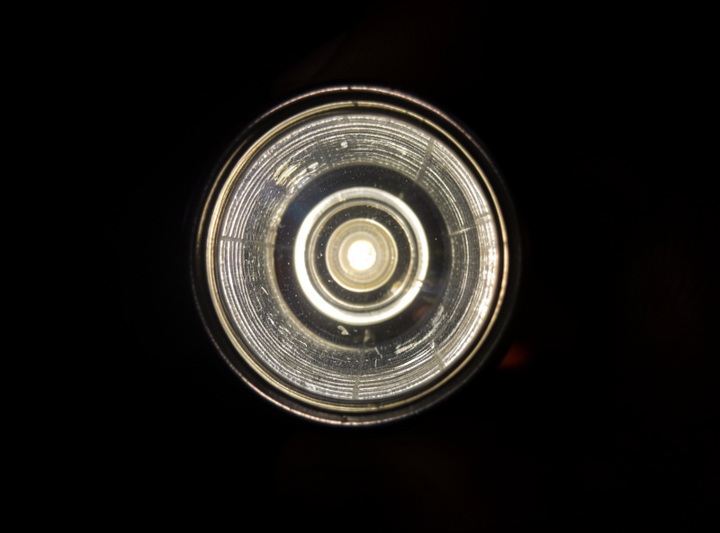 Shining a flashlight through a vintage lens against a dark background to reveal internal fungus