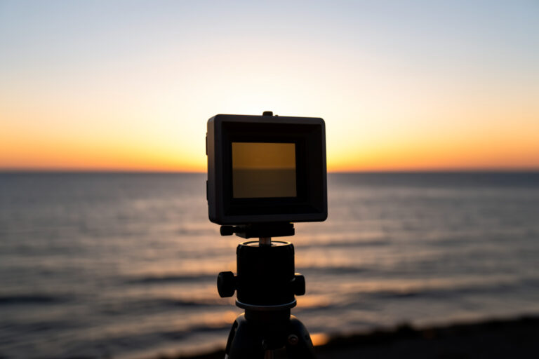 A graduated ND filter in a square holder darkening a bright sky over a sea horizon