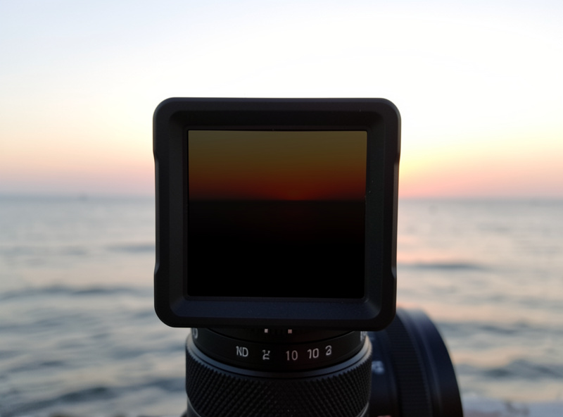 A graduated ND filter sliding into a square holder on a lens, darkening the sky over a flat sea horizon