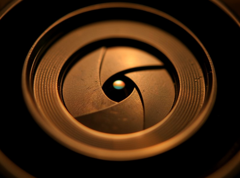 Macro detail of a lens's aperture blades stopped down to f/8 with warm rim light on the metal
