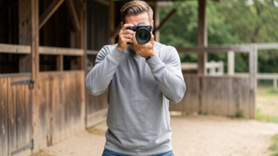 Photographer in a stable wide standing stance with elbows tucked, holding a mirrorless camera to the eye outdoors