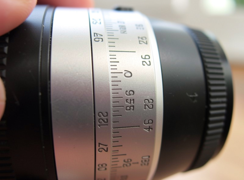 Close-up of an engraved lens barrel depth-of-field and distance scale with a thumb turning the focus ring