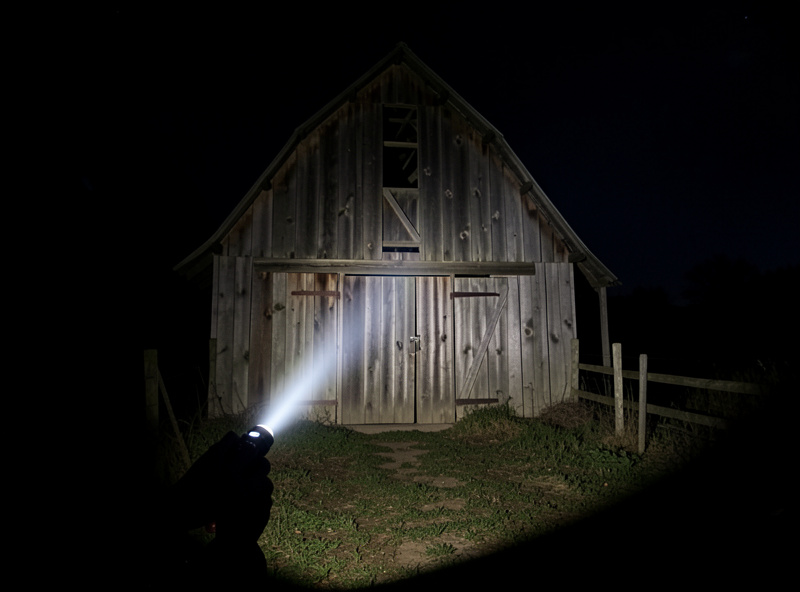 An old wooden barn at night lit selectively by handheld flashlight during a long exposure with pools of light and shadow