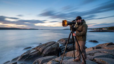 Photographer at a Swedish coastline at blue hour with a tripod-mounted camera and square ND filter