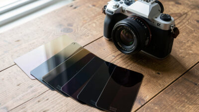 A set of neutral density filters of varying strengths beside a camera and lens