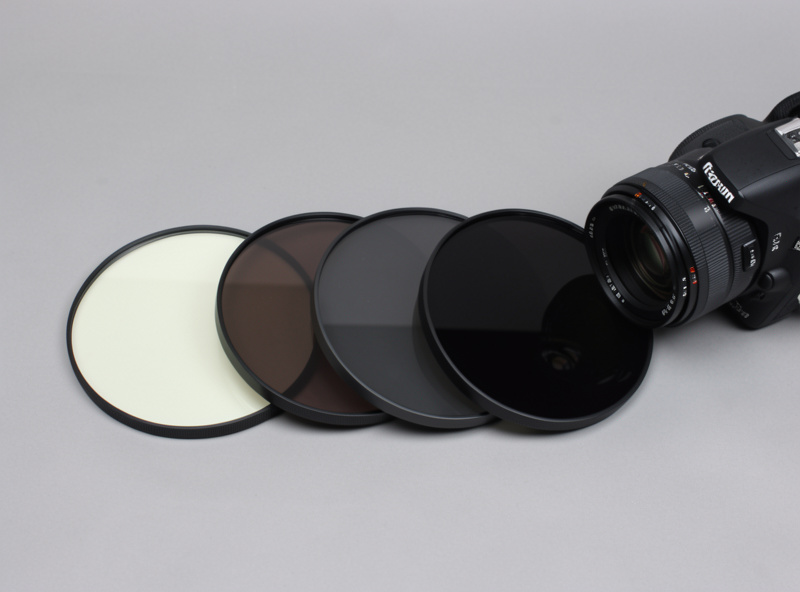 A set of neutral density filters of different strengths fanned out on a table beside a camera