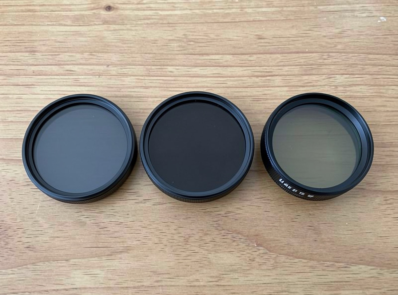 Three fixed ND filters of different strengths beside a variable ND filter on a wooden surface